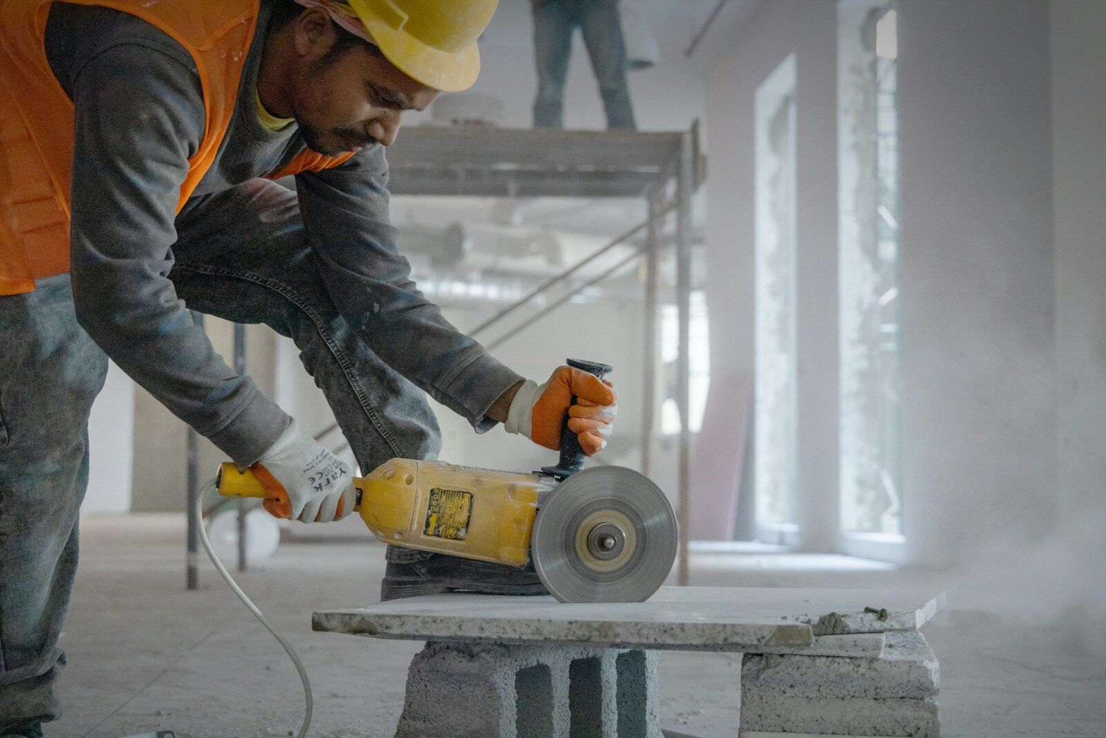 Handwerker mit Schutzhelm und Handschuhen arbeitet mit einem Trennschleifer auf einer Baustelle.