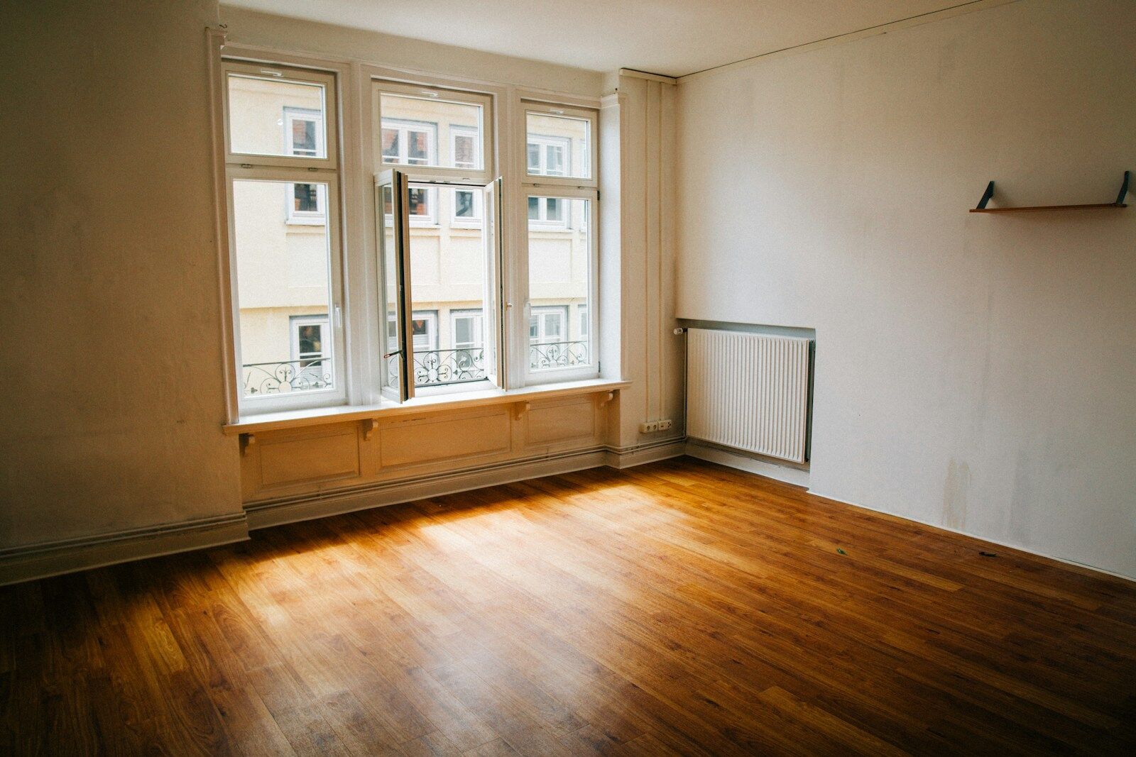 Heller, leerer Wohnraum mit Holzboden und großen Fenstern.